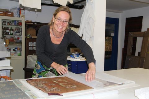 Ein besticktes Seidentextil wird behutsam mit einer Schutzfolie abgedeckt.