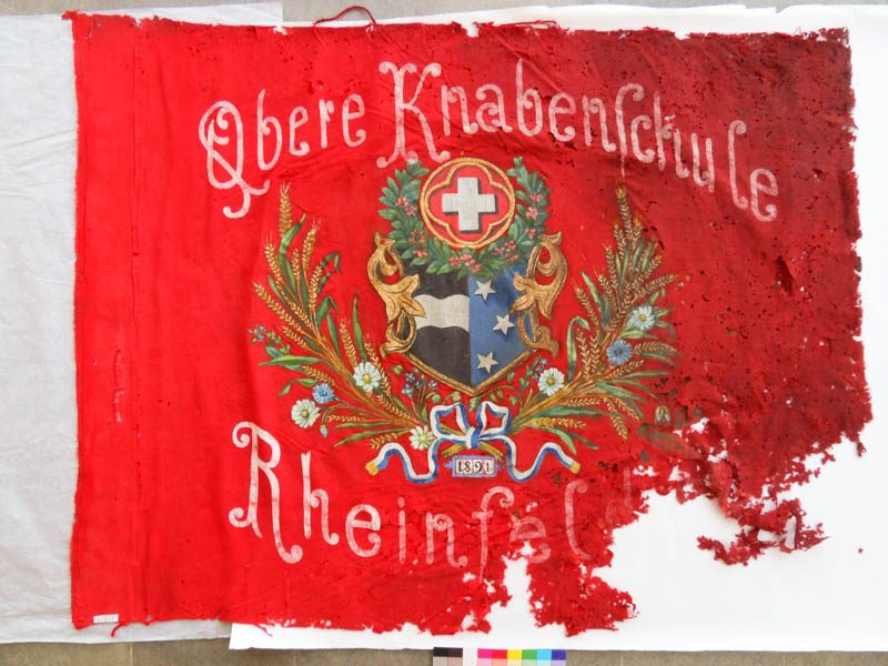 Stark zerschlissene rote Fahne der Oberen Knabenschule Rheinfelden von 1891 mit grossen Fehlstellen.