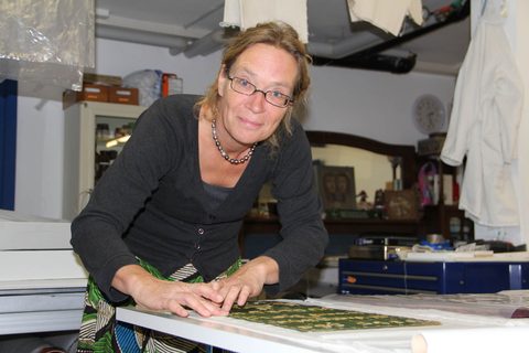 Arbeit an einem grünen Textil mit goldener Metallfadenstickerei.