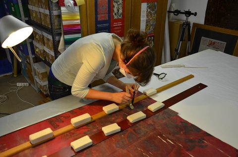 Eine bemalte rote Fahne wird mit Pinsel gefestigt und mit Gewichten beschwert.
