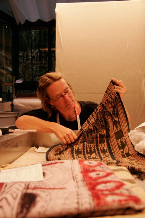 Restauratorin begutachtet ein gemustertes Ikat-Gewebe mit Fransen.